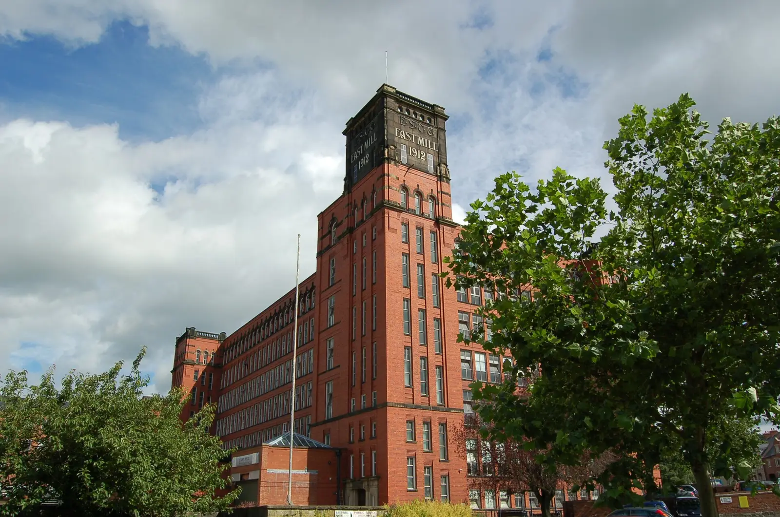 The East Mill water tower and red-brick elevation behind trees.
